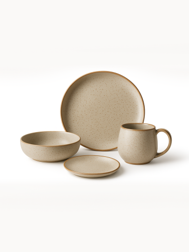 Minimalistyczny zestaw naczyń kamionkowych o nakrapianym, beżowym wykończeniu z naturalnym brązowym rantem jest ułożony na jednolitym białym tle. Kolekcja zawiera duży talerz obiadowy, średnią miskę, mały spodek oraz pasujący kubek.