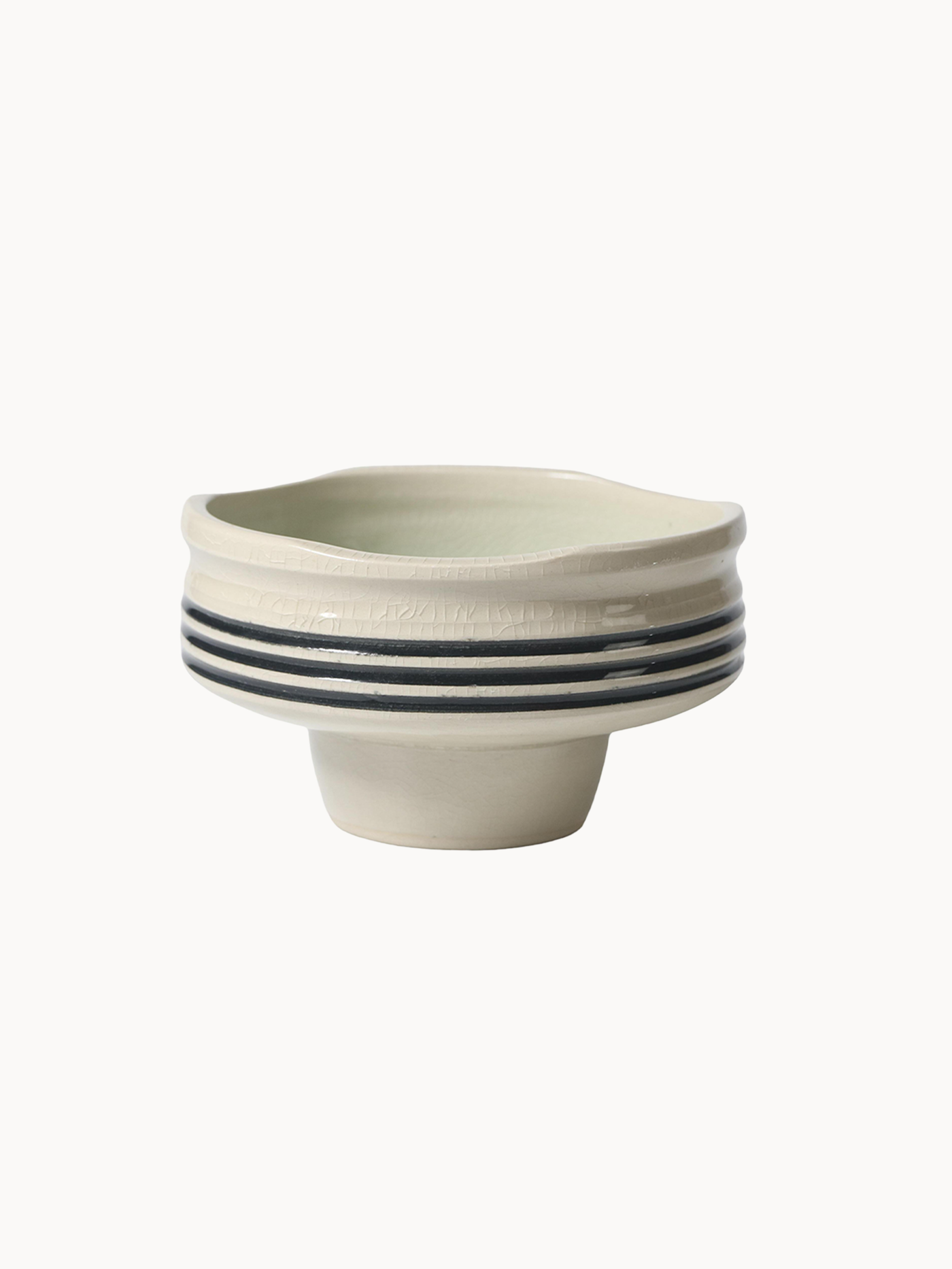Ceramiczna miska na podwyższeniu w jasnokremowym kolorze, pokryta spękanym szkliwem z trzema czarnymi paskami wokół środka.